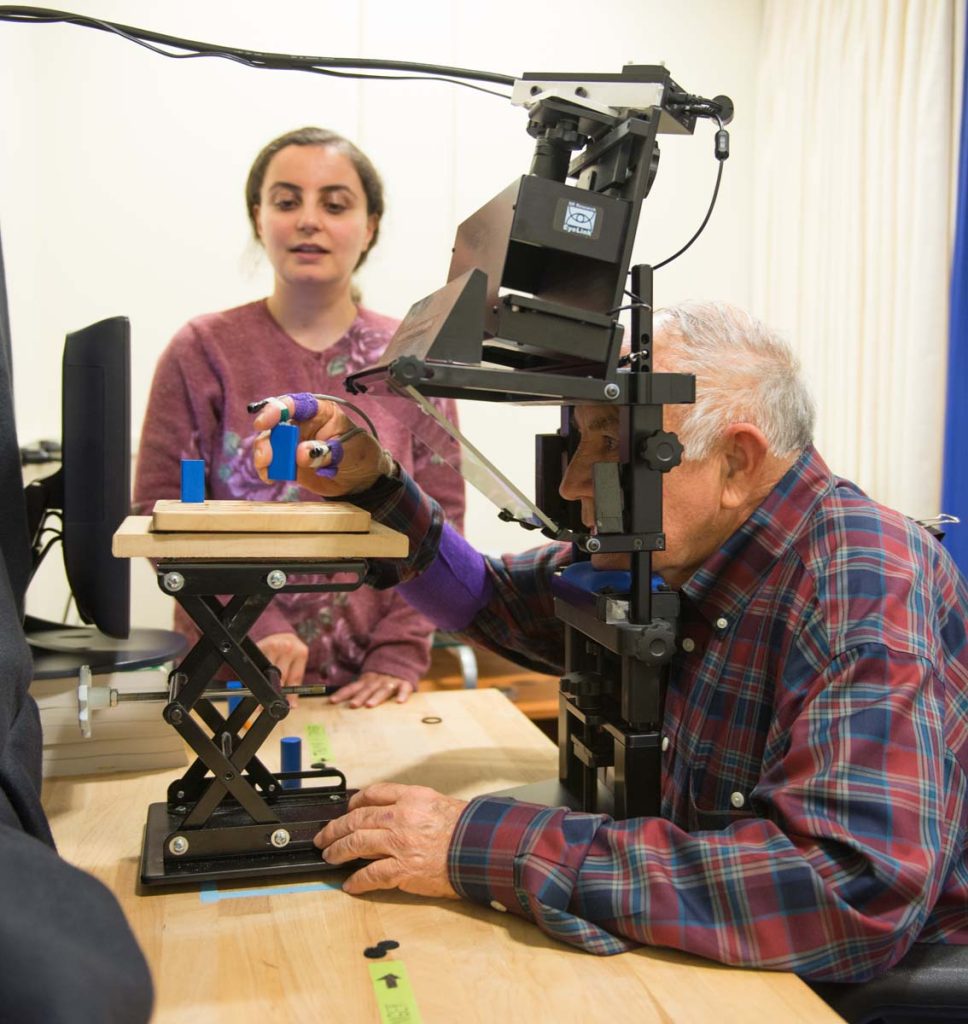 man seated in an eye tracking device holding a peg he is about to place into a hole on the beg board in front of him
